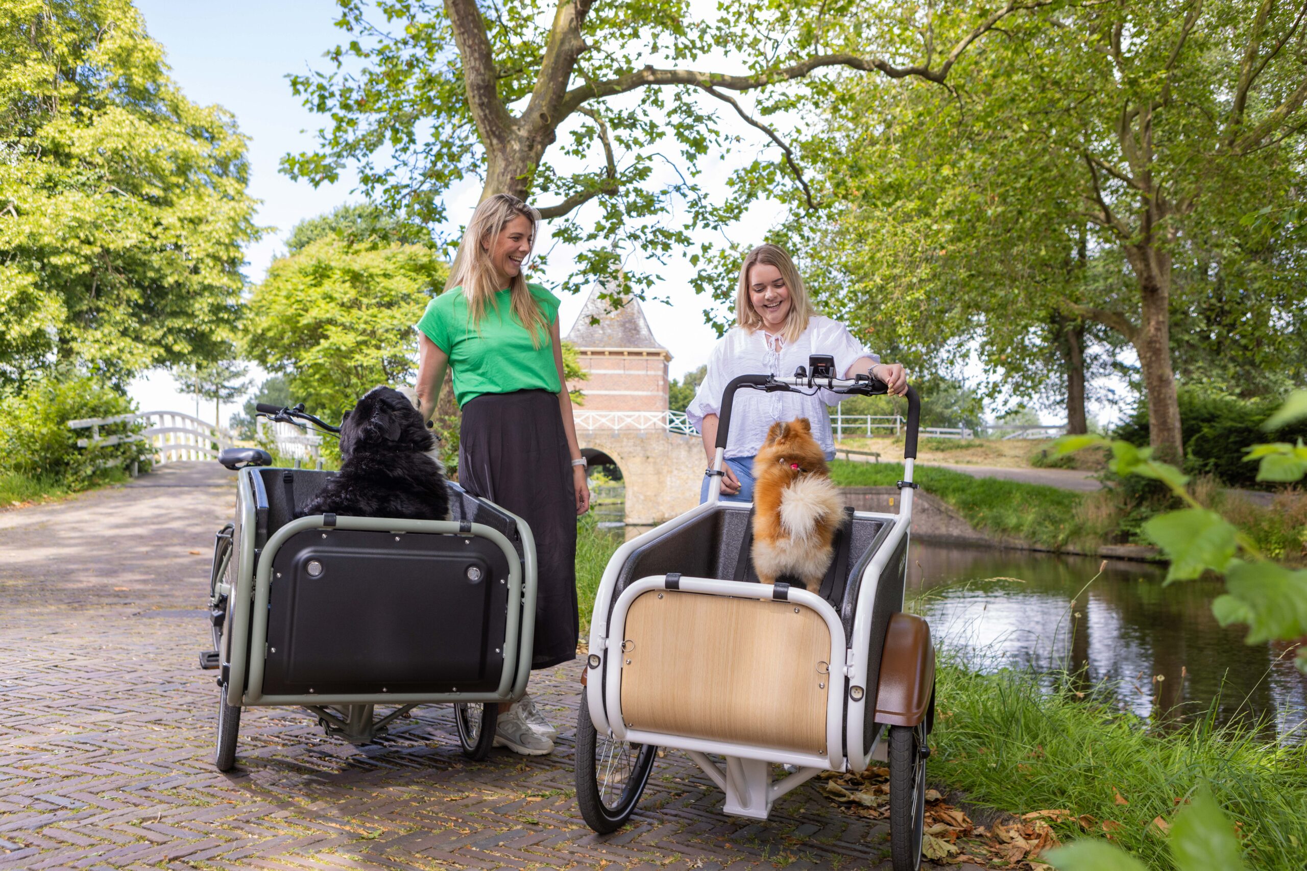 Een SociBike Family en een SociBike Compact met de berijders naast de bakfiets en in beiden bakfietsen een hond